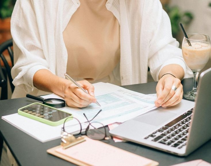 Mãos preenchendo uma planilha financeira ao lado da calculadora