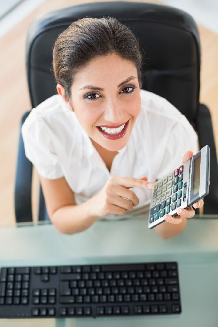 Mulher sorrindo com calculadora na mesa de trabalho